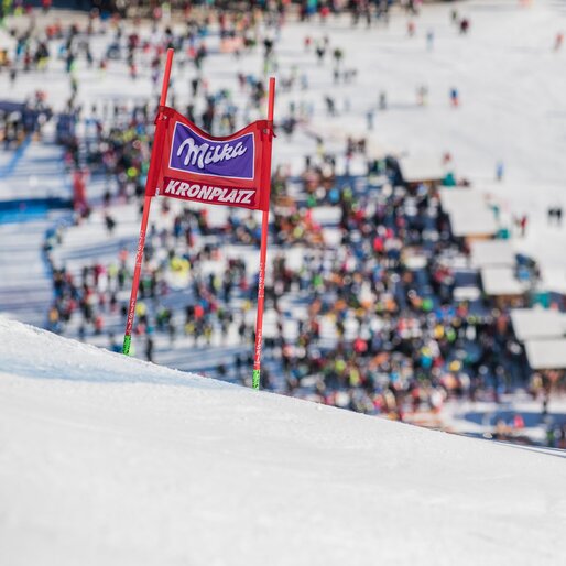 Ein Slalomtor mit der Aufschrift "Milka" und "Kronplatz", im Hintergrund die Menschenmasse am Zieleinlauf. | © Harald Wisthaler