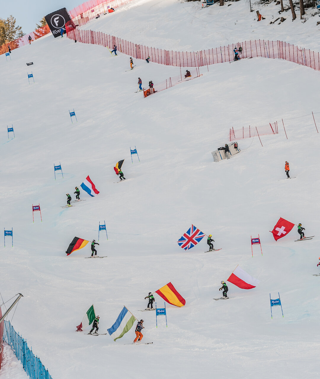 Skifahrer mit den Fahnen verschiedener Länderflaggen fahren den Riesenslalom hinab. | © Harald Wisthaler