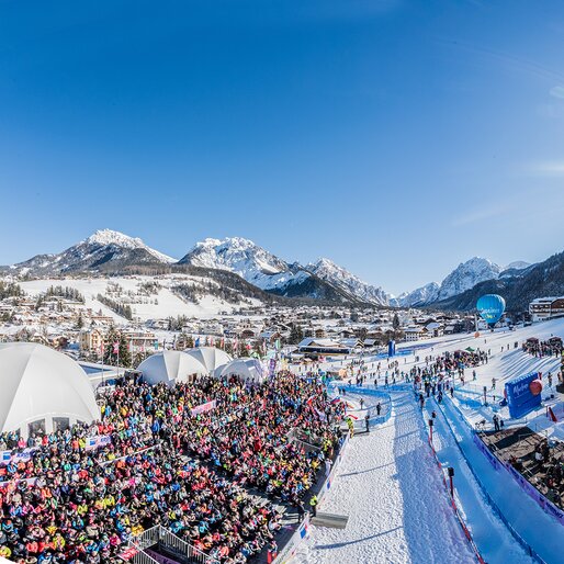 Der Zielbereich eines Skirennens mit den Zuschauerrängen und dem strahlend blauen Himmel und Bergpanorama im Hintergrund. | © Harald Wisthaler