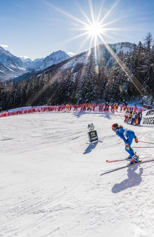 Eine Skirennläuferin startet den Riesenslalom und wird von Zuschauern am Rande der Piste bejubelt, im Hintergrund das Bergpanorama und strahlend blauer Himmel. | © Harald Wisthaler