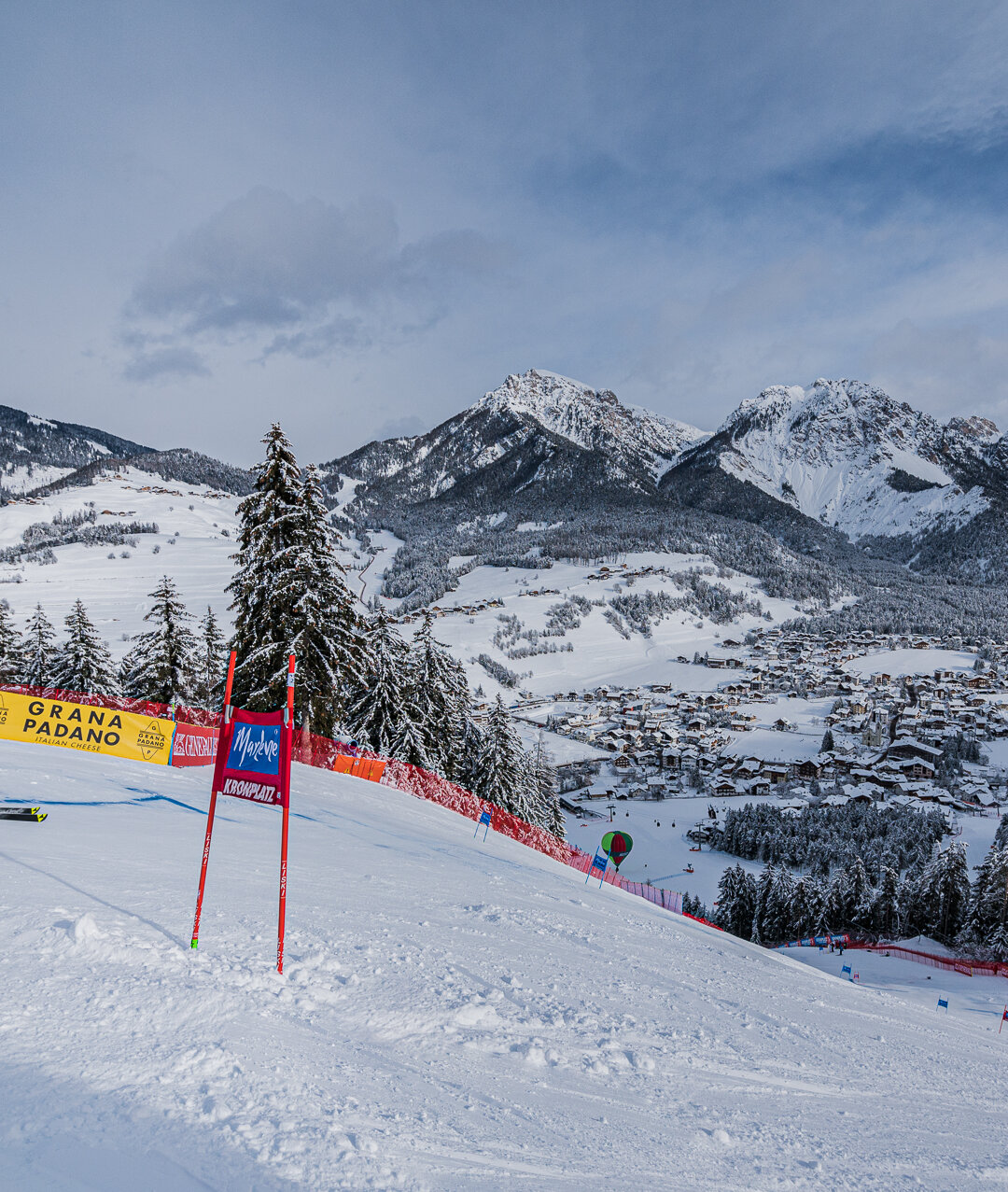 Eine Skirennläuferin fährt um ein Slalomtor, dahinter das verschneite Bergpanorama. | © Harald Wisthaler