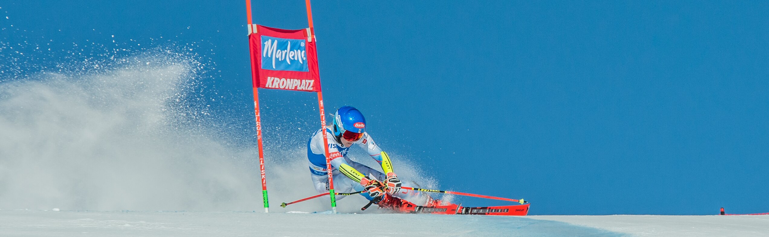 Eine Skirennläuferin fährt unter blauem Himmel durch ein Slalomtor. | © Gianvito Coco