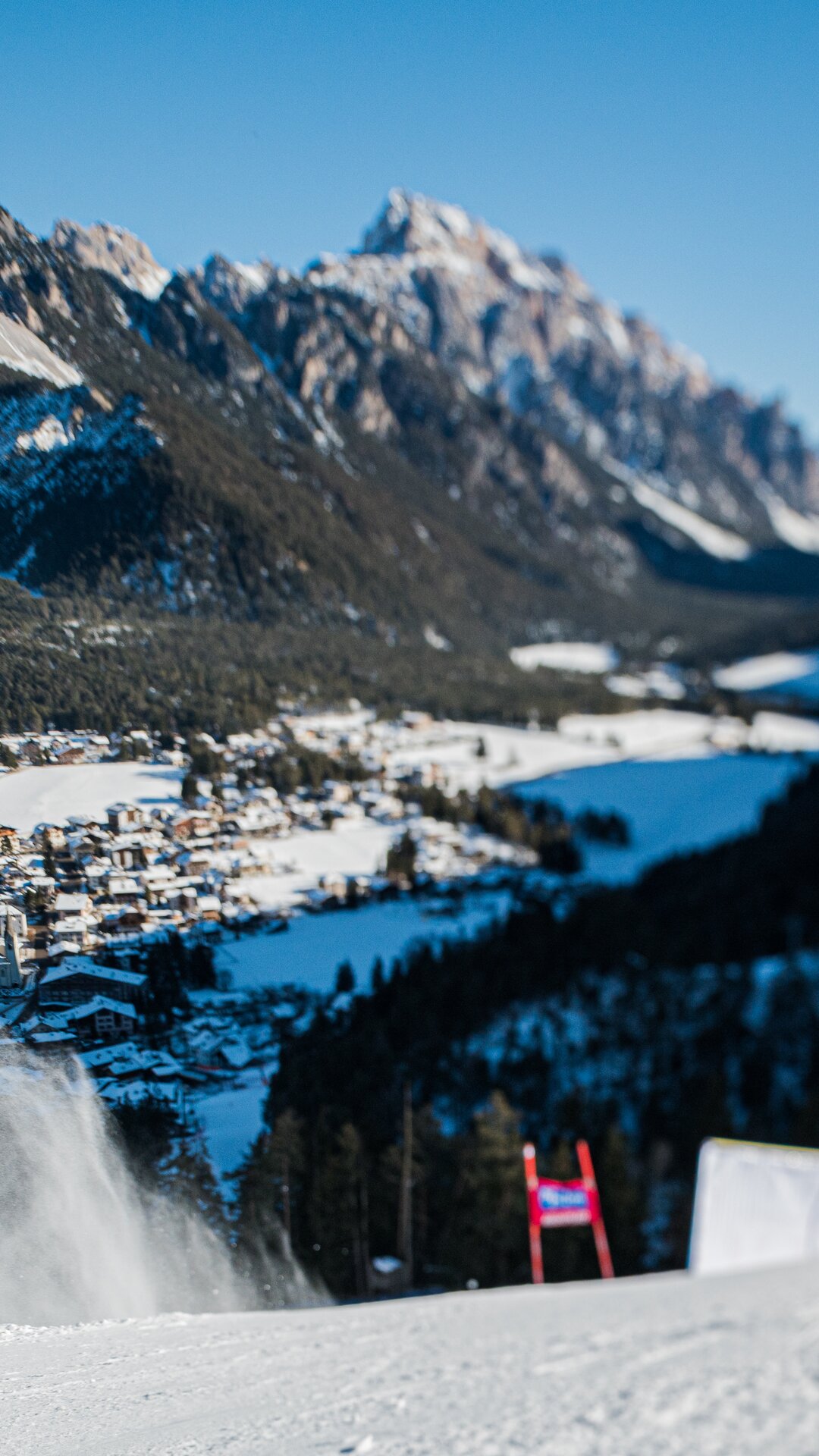 Eine Skirennstrecke mit aufgewirbeltem Schnee vor dem Hintergrund eines verschneiten Tals, Bergen und blauem Himmel. | © Harald Wisthaler