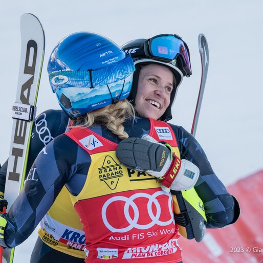 Zwei Skirennläuferinnen umarmen sich nach dem Rennen und halten ihre Ski in den Händen. | © Gianvito Coco