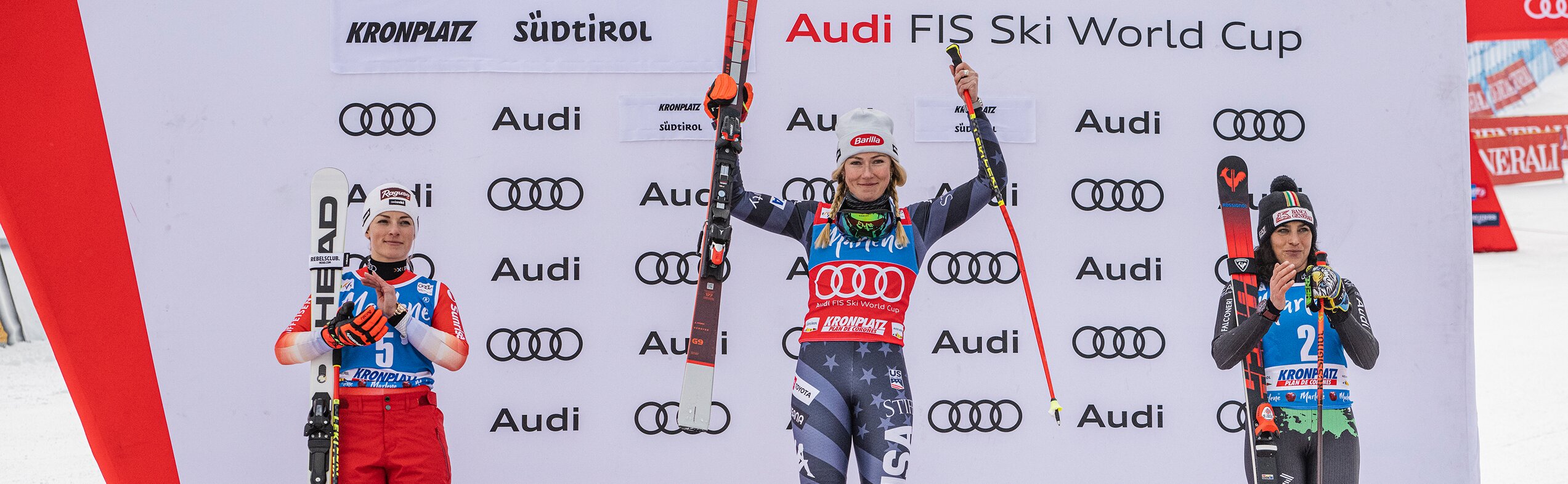 Drei Skirennläuferinnen stehen auf dem Podest, die äußeren beiden klatschen während die mittlere jubelnd ihre Ski in die Höhe hält. | © Harald Wisthaler