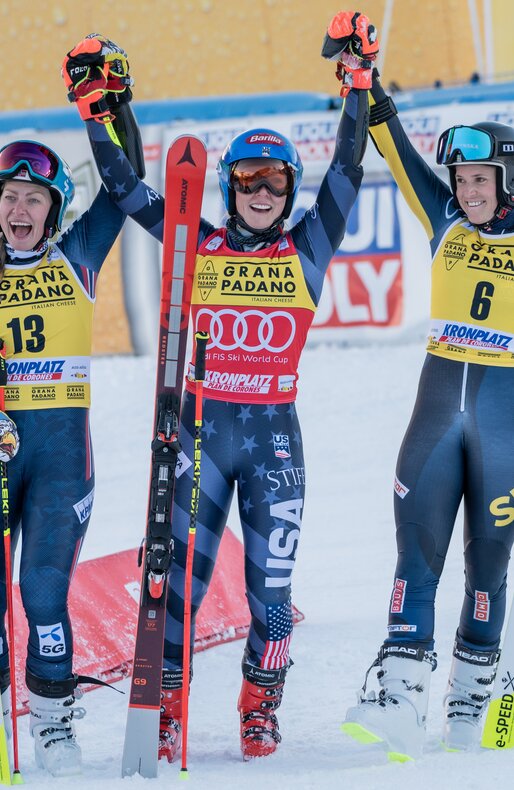 Drei Skirennläuferinnen stehen neben dem Podests und jubeln mit winkenden Armen. | © Gianvito Coco