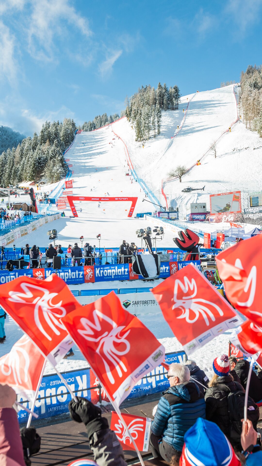 Der Zieleinlauf mit Zuschauerrängen eines Skirennens vor dem Hintergrund der Piste und anderer verschneiter Berge. | © Gianvito Coco
