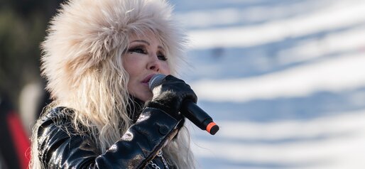 Eine Sängerin mit großer Fellmütze singt leidenschaftlich ins Mikrofon, im Hintergrund die verschneite Skipiste. | © Gianvito Coco