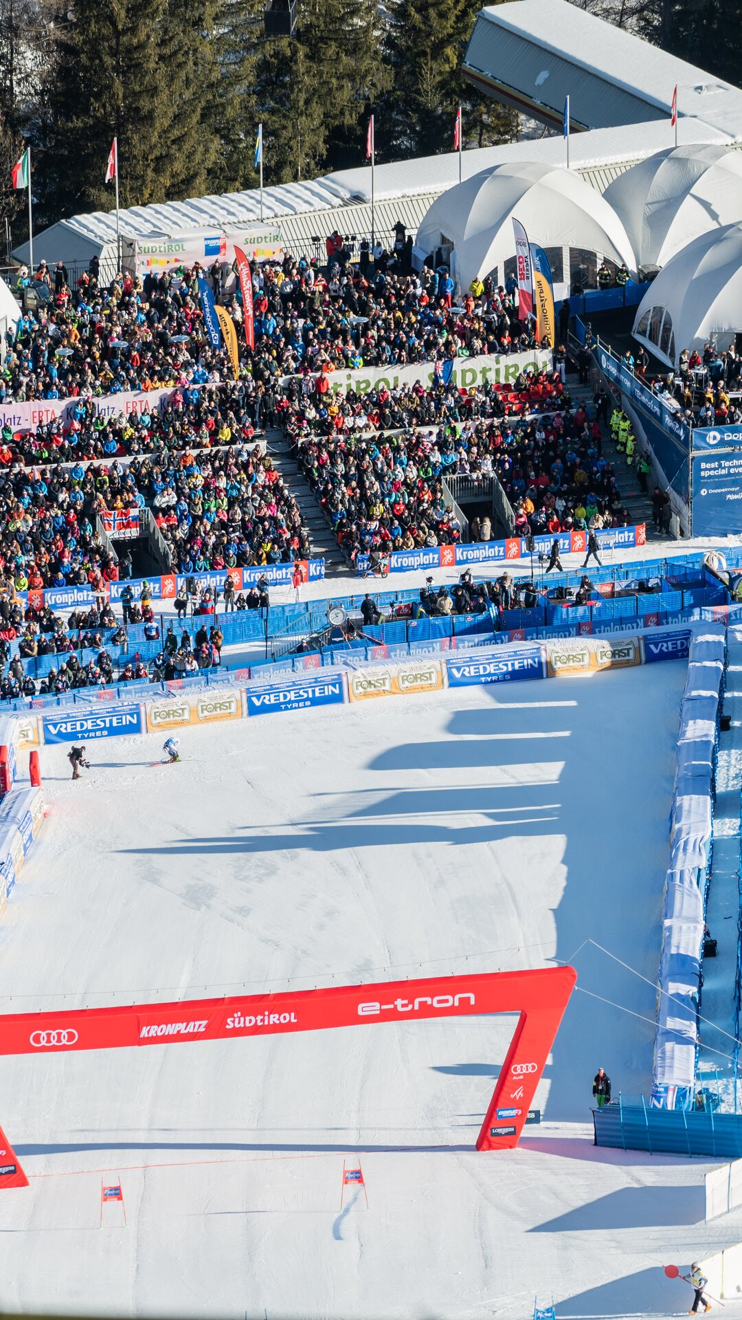 Die Zielarena ist dicht gefüllt mit Zuschauertribünen und einer abgesperrten Skipiste. | © Gianvito Coco