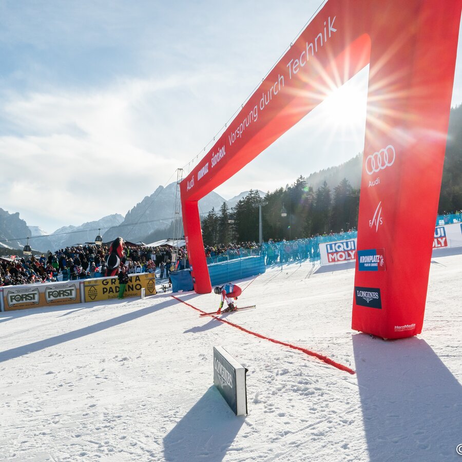 Eine Rennläuferin kommt in den Zielbereich, im Hintergrund strahlendes Wetter und jubelnde Zuschauer. | © Mattia Negrini