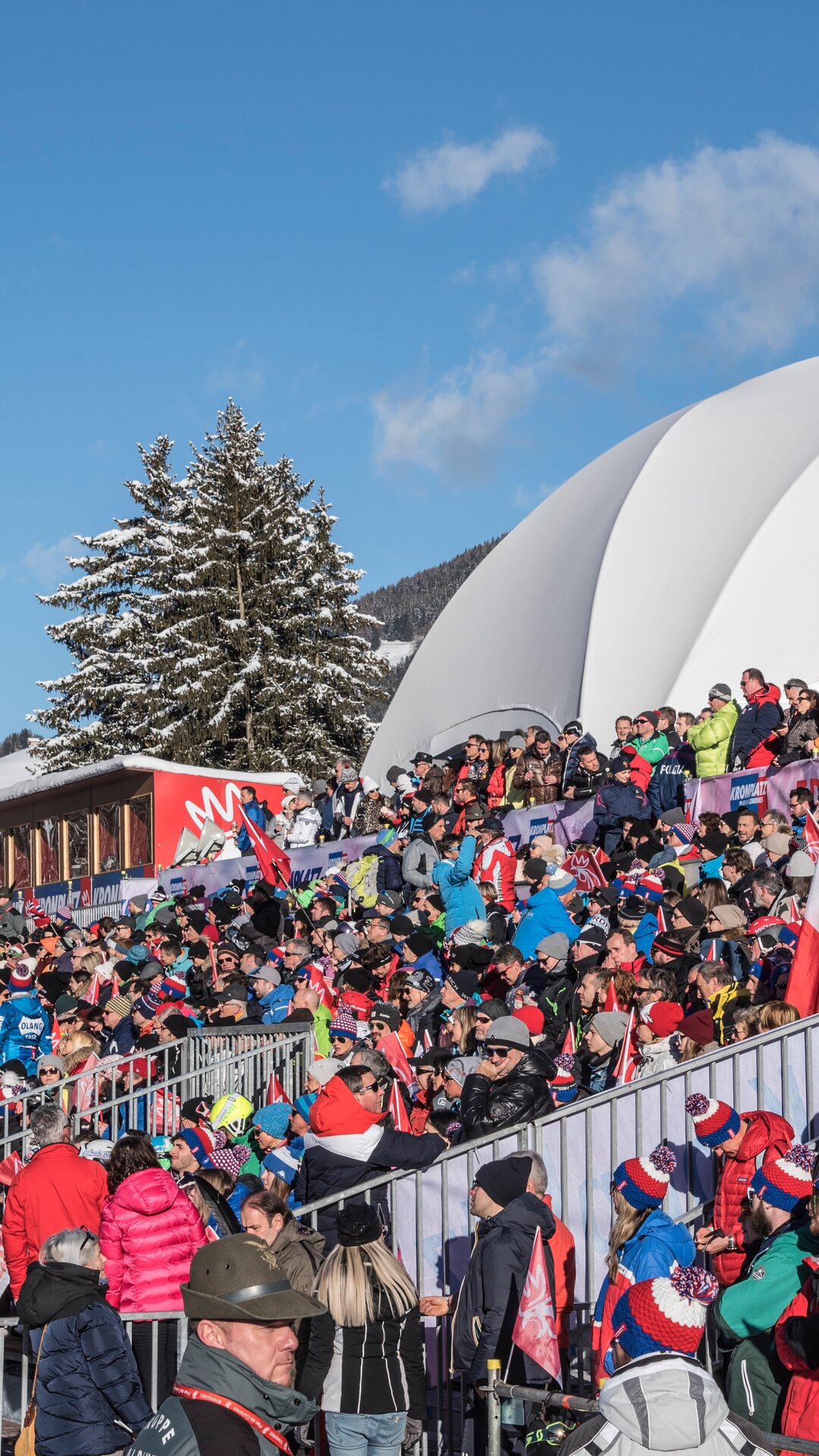 Eine Tribüne voller Zuschauer bei blauem Himmel im Winter | © Skirama Kronplatz