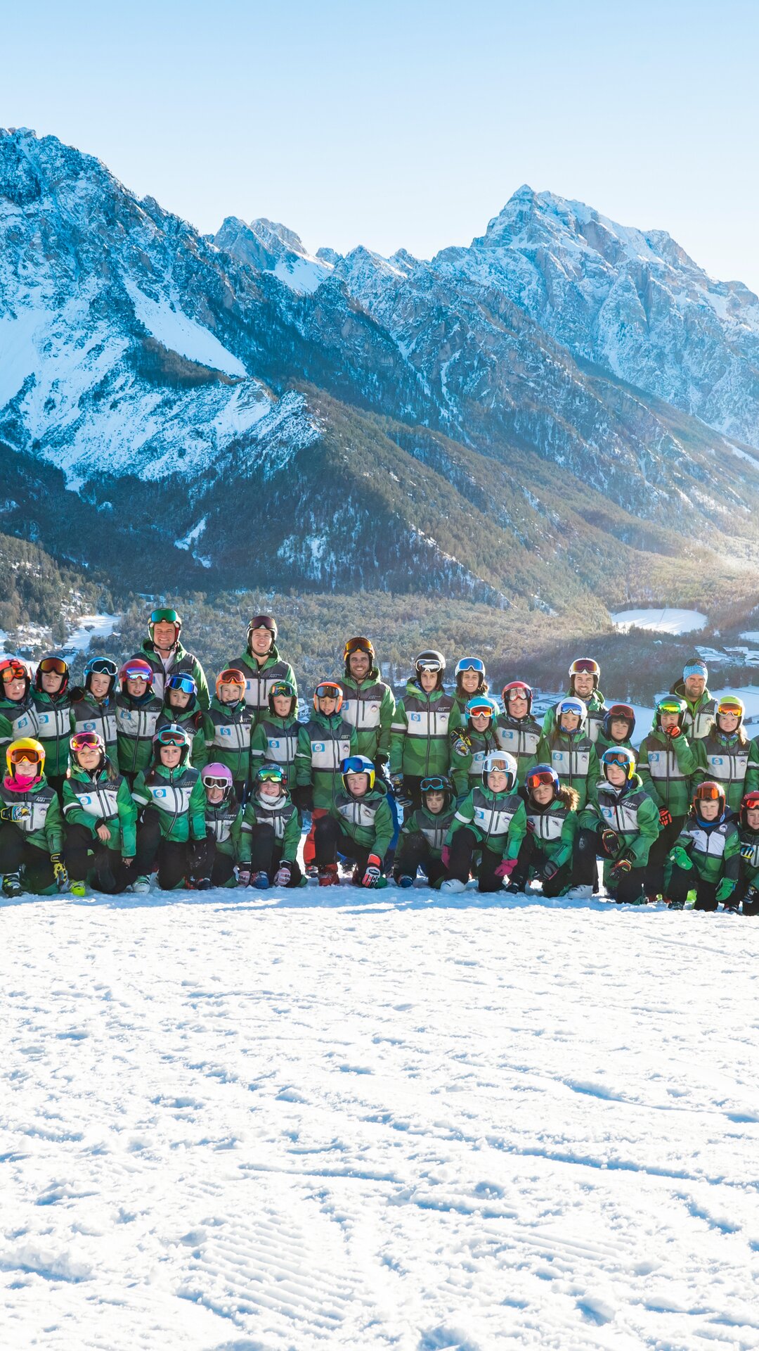 Gruppenfoto eines Ski Clubs auf einer Skipiste, im Hintergrund das Bergpanorama und strahlend blauer Himmel. | © Ski Club San Vigilio
