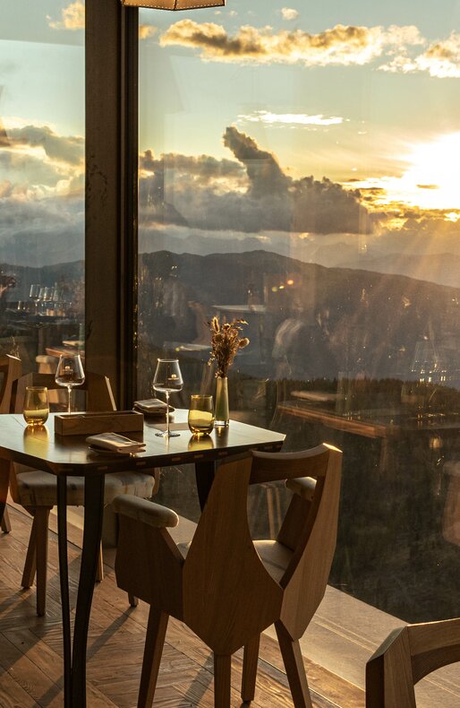 Ein leerer Tisch und zwei leere Stühle im AlpiNN Restaurant bei Sonnenuntergang. | © Skirama Kronplatz