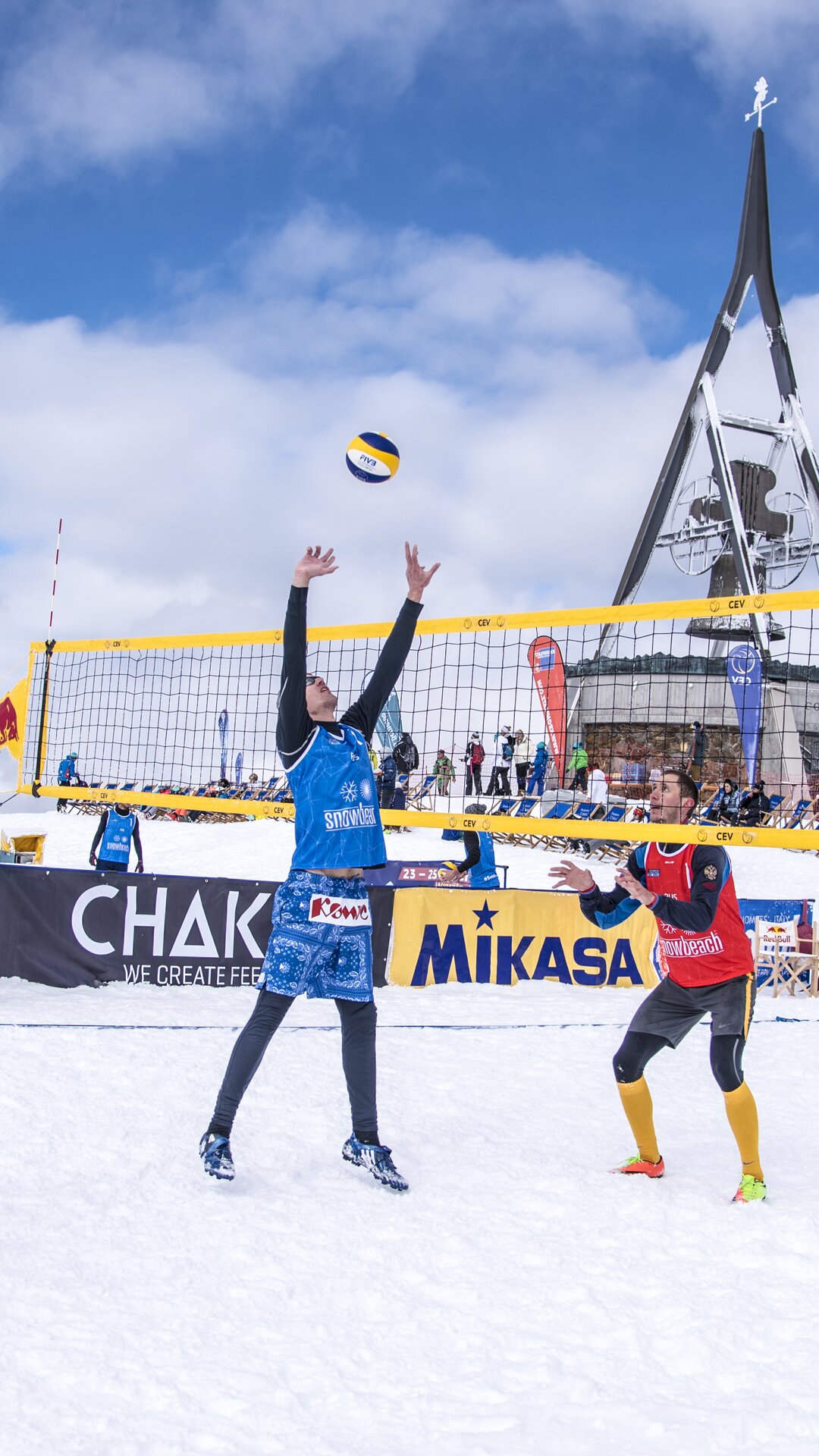 Mehrere Personen beim Snowvolleyball spielen bei bewölktem Himmel und der Concordia 2000 Glocke im Hintergrund. | © Skirama Kronplatz