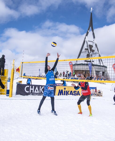 Mehrere Personen beim Snowvolleyball spielen bei bewölktem Himmel und der Concordia 2000 Glocke im Hintergrund. | © Skirama Kronplatz
