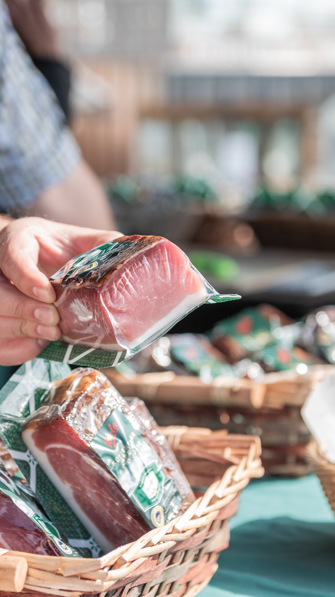 Ein Verkäufer reicht ein Stück vakuumverpackten Speck über einen Marktstand. | © Gianvito Coco
