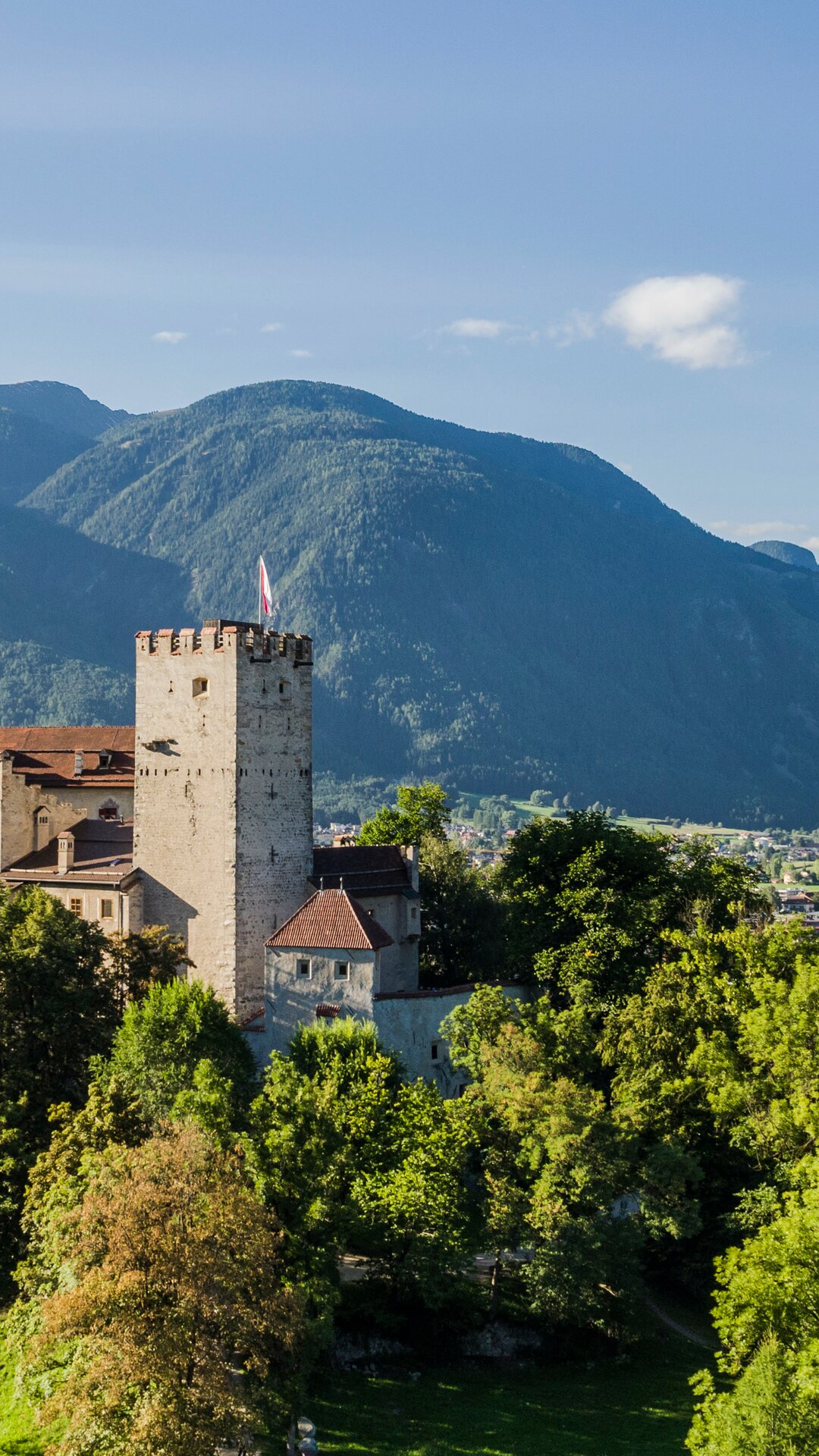Das Schloss Bruneck im Sommer umrundet von grünen Bäumen und Wiesen bei blauem Himmel. | © Harald Wisthaler
