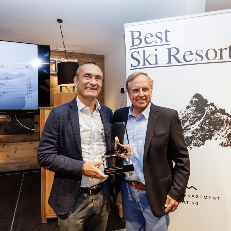 Zwei Männer halten einen Preis in den Händen, im Hintergrund ein Aussteller mit der Aufschrift "Best Ski Resort". | © Skirama Kronplatz