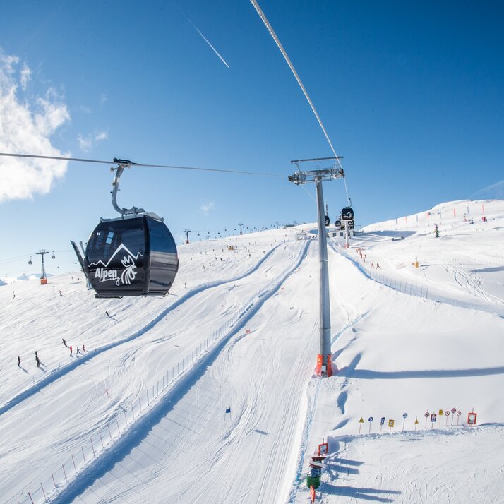 Eine Gondelbahn vor dem Hintergrund einer Skipiste und blauem Himmel.  | © Harald Wisthaler