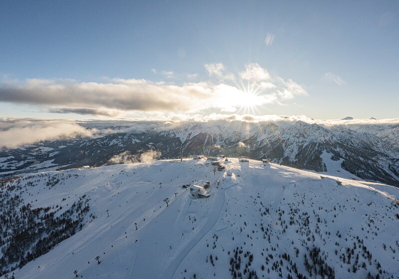 Sonnenstrahlen brechen durch die Wolken über einem verschneiten Berghang mit Skiliften. | © Harald Wisthaler